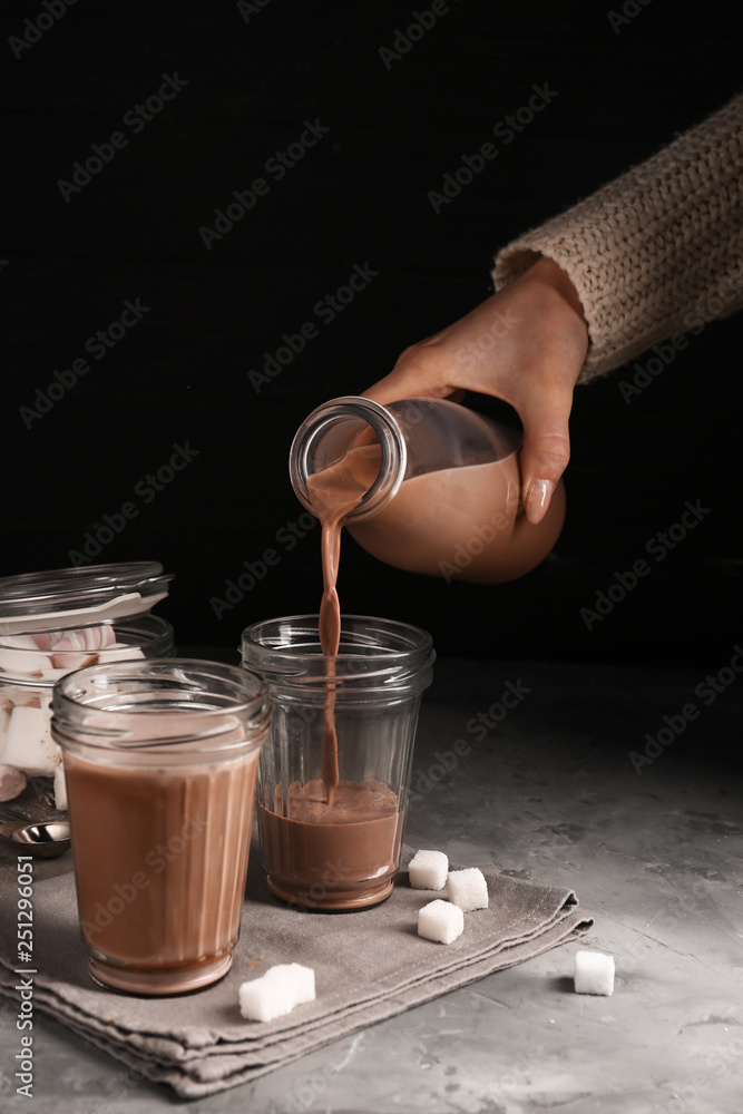 Pouring of tasty cacao drink from bottle into glass on table