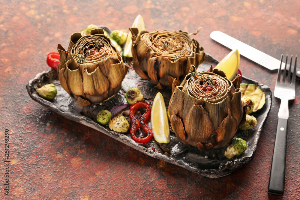 Plate with tasty baked artichokes and vegetables on table