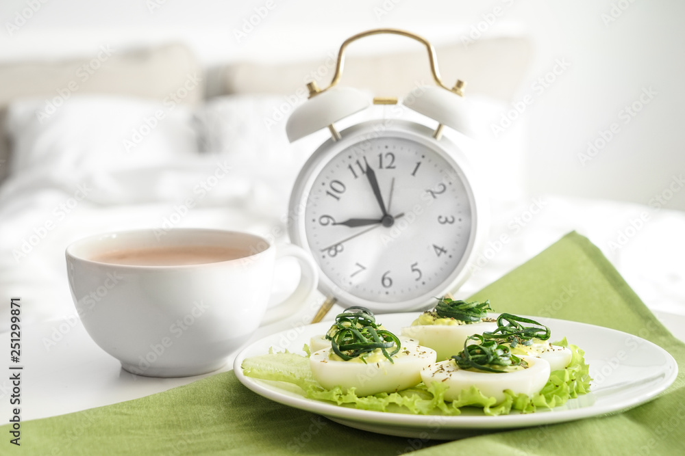 Plate with tasty deviled eggs and cup of coffee on bed