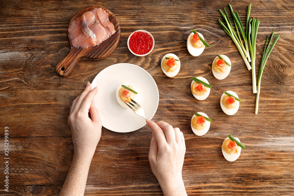 Woman eating tasty deviled eggs on wooden table