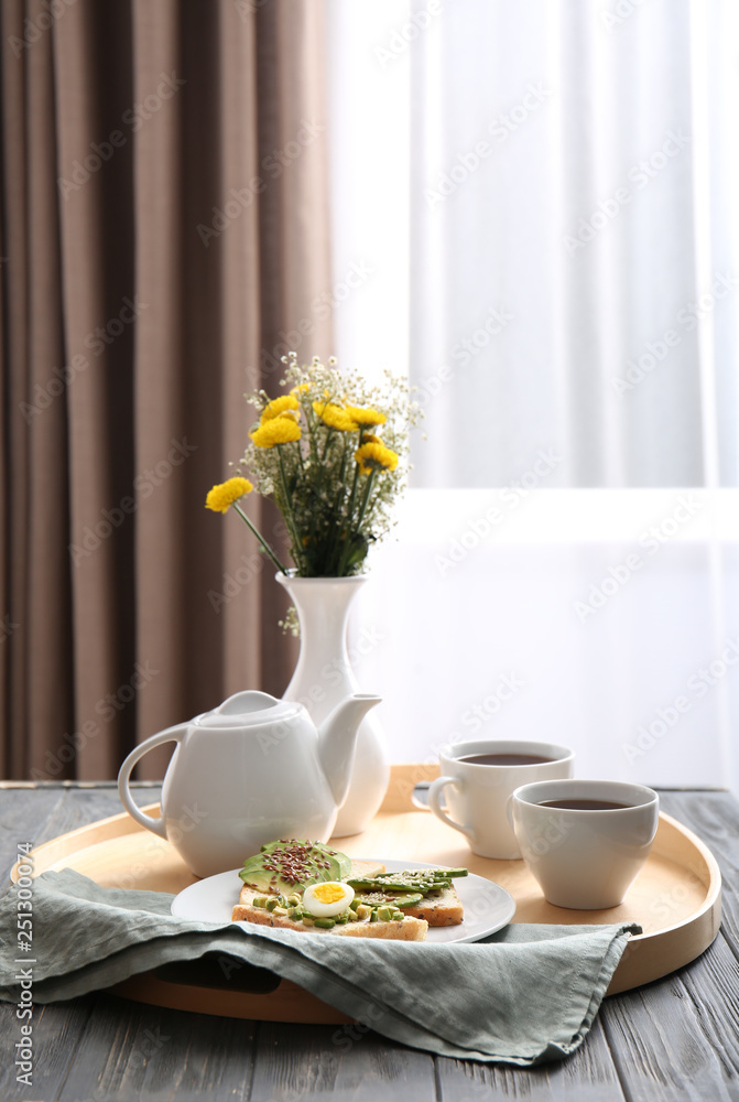 Tray with tasty avocado sandwiches and tea on table in room