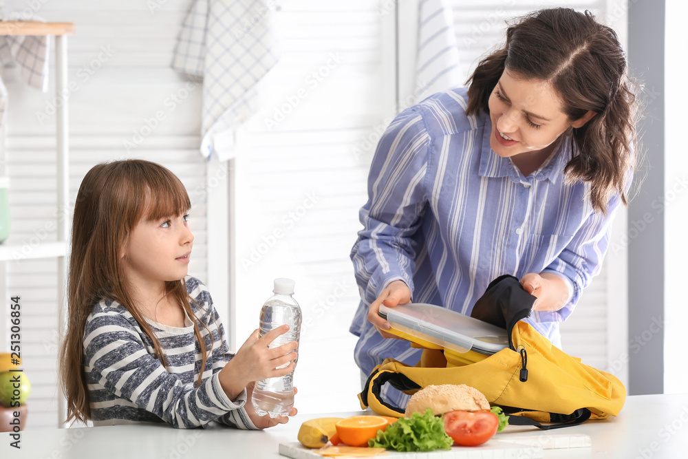 Mother with cute daughter packing lunch into backpack at home