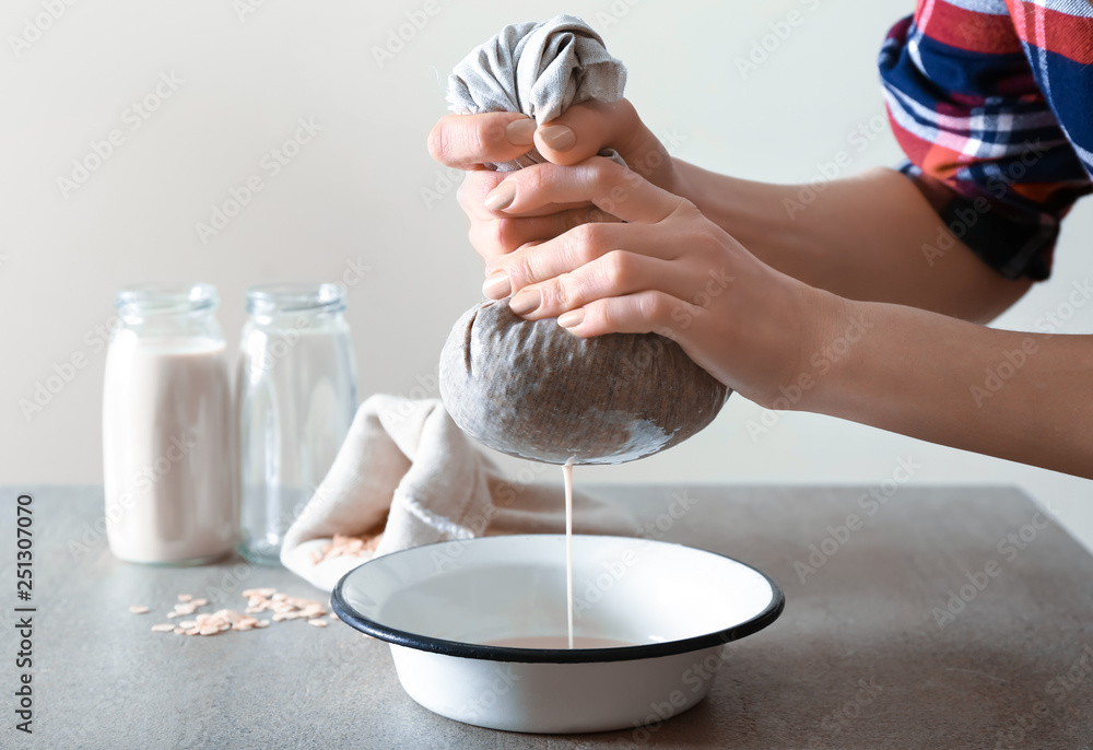 Woman preparing tasty oat milk on table