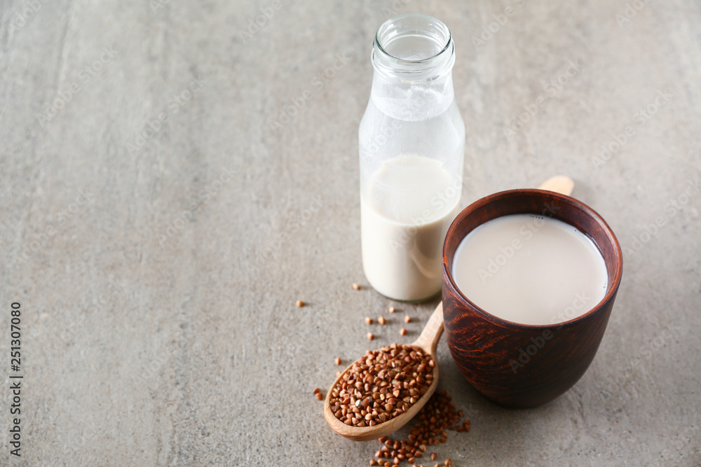 Cup and bottle of tasty buckwheat milk on grey table