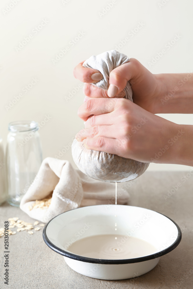 Woman preparing tasty oat milk on table