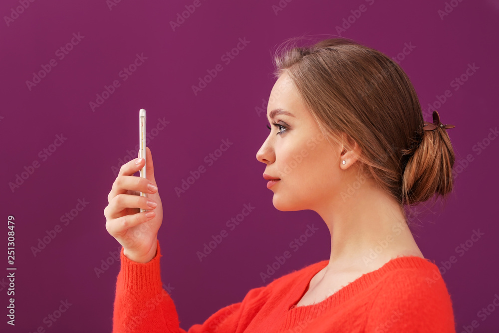 Young woman taking selfie with mobile phone on color background