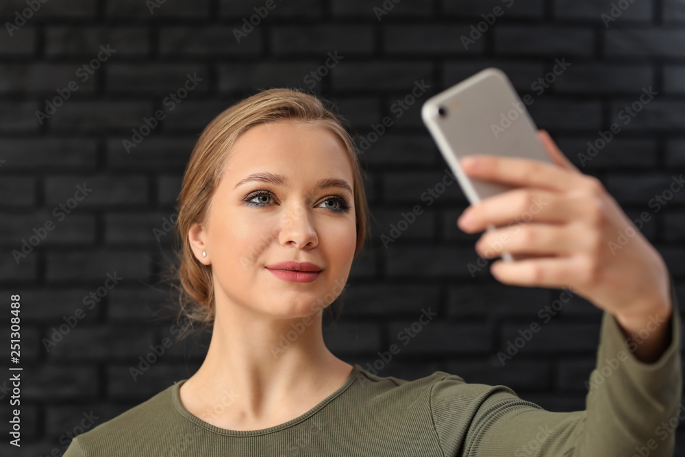 Young woman taking selfie with mobile phone on dark brick background