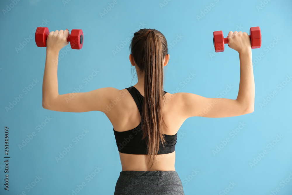 Sporty young woman with dumbbells on color background