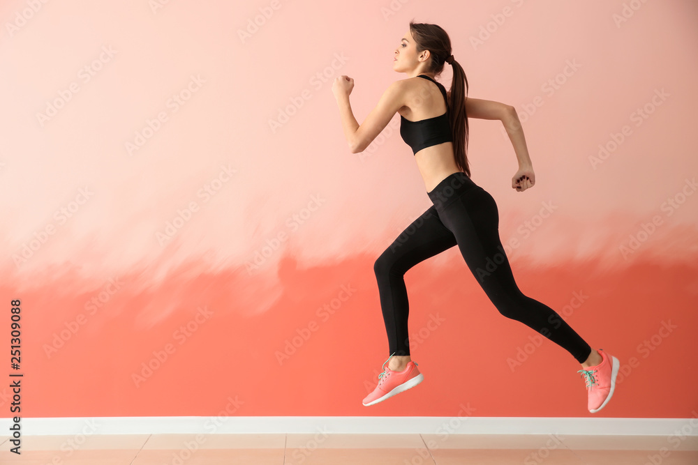 Sporty young woman running against color wall