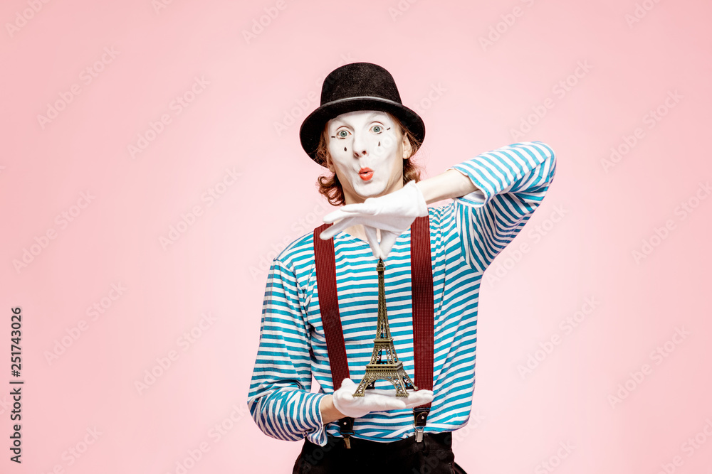 Pantomime with white facial makeup posing with Eiffel tower on the pink background. French mime conc