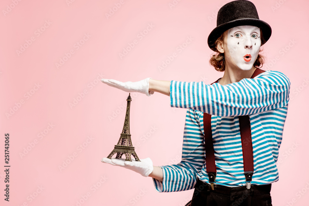 Pantomime with white facial makeup posing with Eiffel tower on the pink background. French mime conc