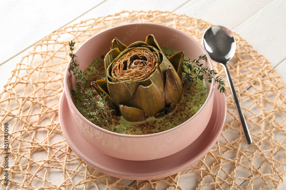 Bowl with tasty cream soup and artichoke on table