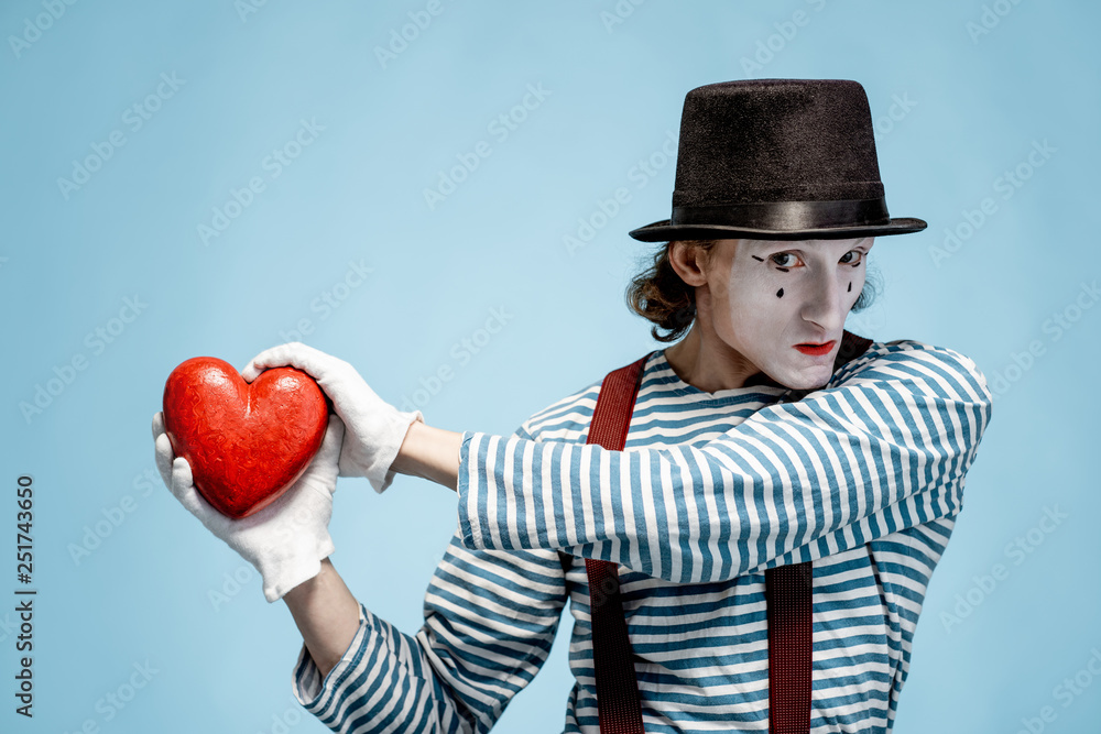 Portrait of an actor as a pantomime with white facial makeup posing with red heart on the blue backg