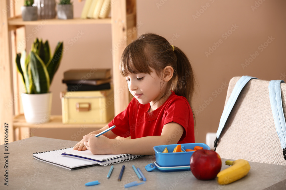 Little girl with lunch box sitting in classroom