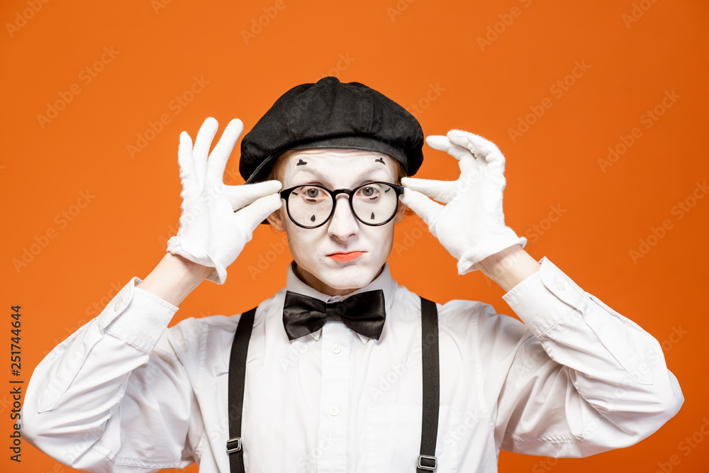 Portrait of a pantomime with white facial makeup in eyeglasses showing expressive emotions on the or