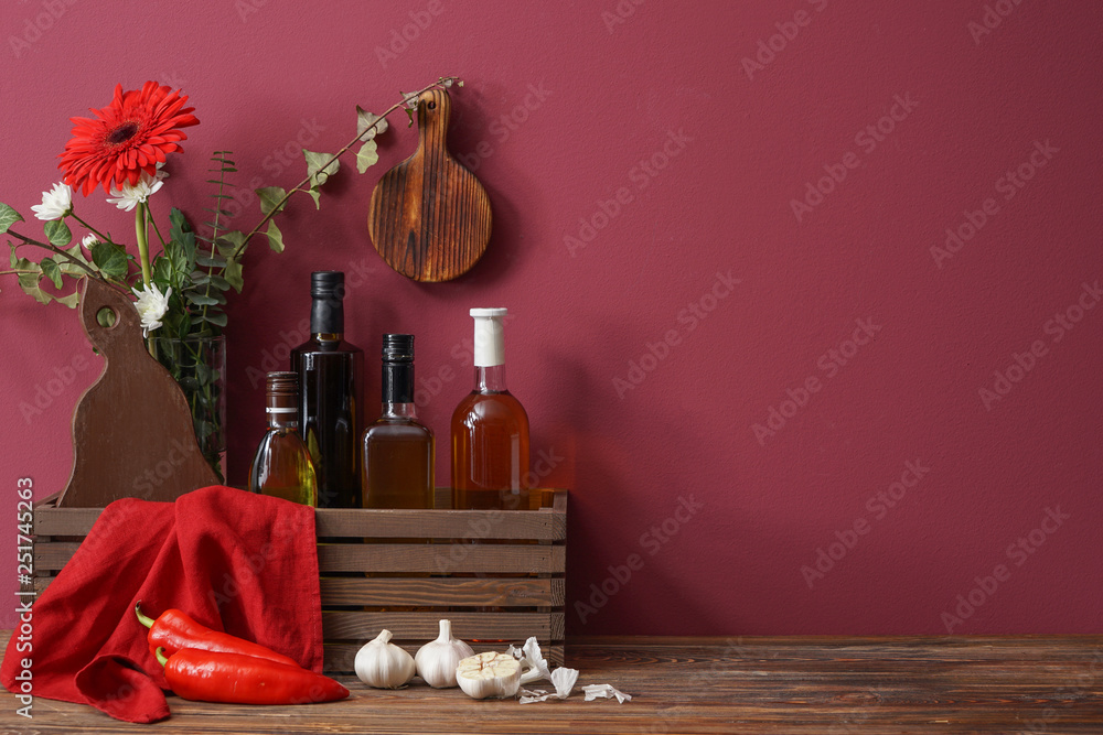 Wooden box with bottles of oil and vegetables on table near color wall