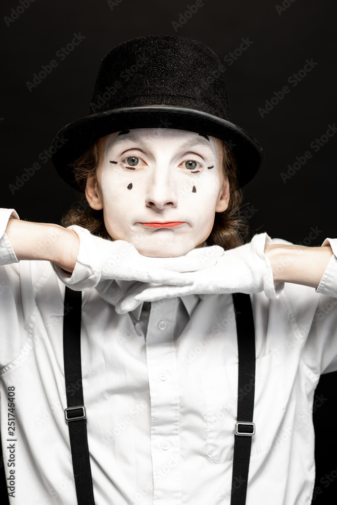 Close-up portrait of a pantomime with white facial makeup posing with expressive emotions on the bla