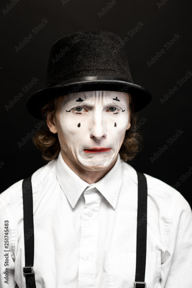 Close-up portrait of a pantomime with white facial makeup posing with expressive emotions on the bla