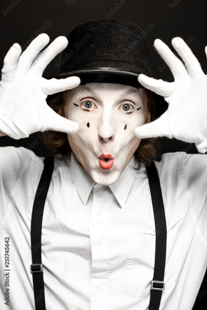 Close-up portrait of a pantomime with white facial makeup posing with expressive emotions on the bla