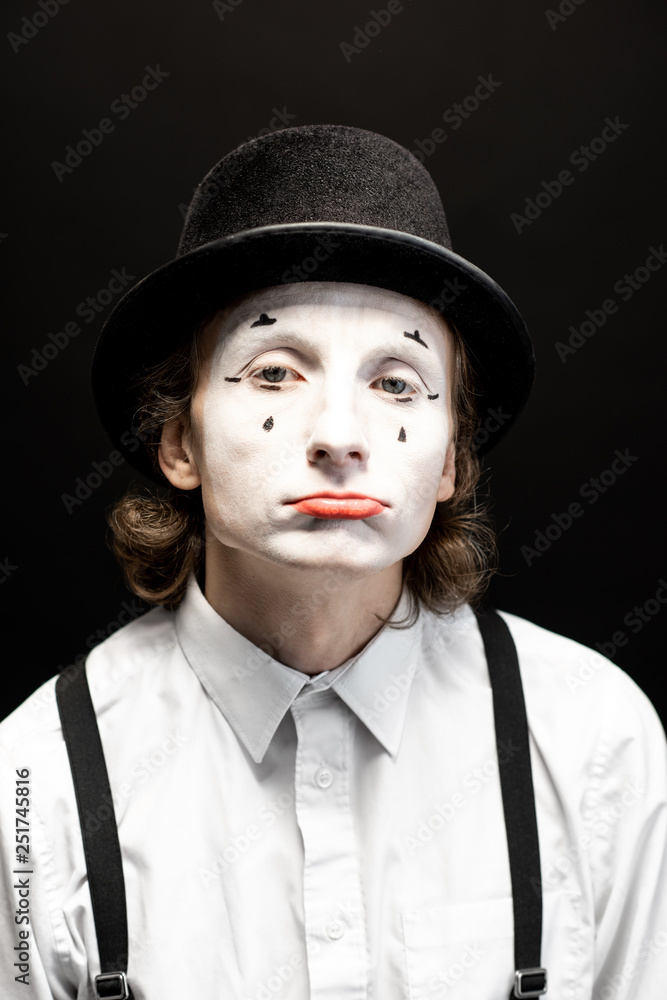 Close-up portrait of a pantomime with white facial makeup posing with expressive emotions on the bla