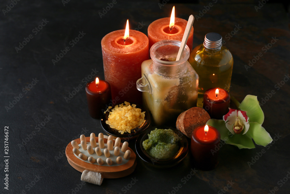 Beautiful burning candles with cosmetic products on dark background