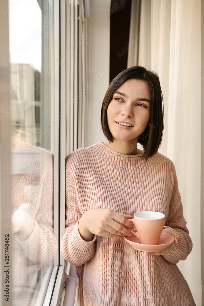 年轻女子早上在窗户附近喝咖啡