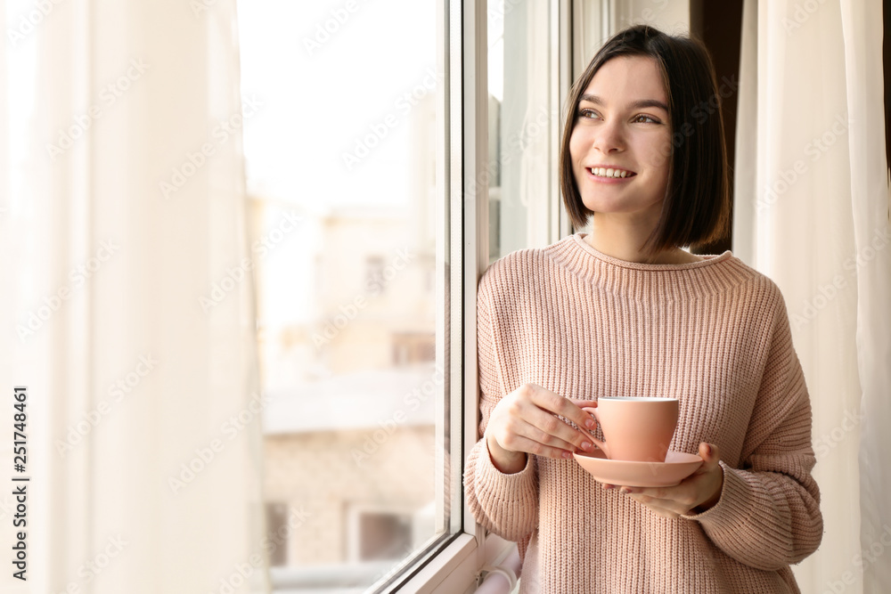 年轻女子早上在窗户附近喝咖啡