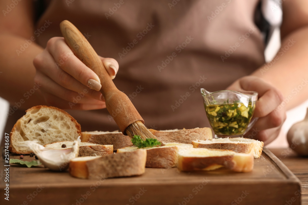 Woman making tasty garlic bread in kitchen, closeup