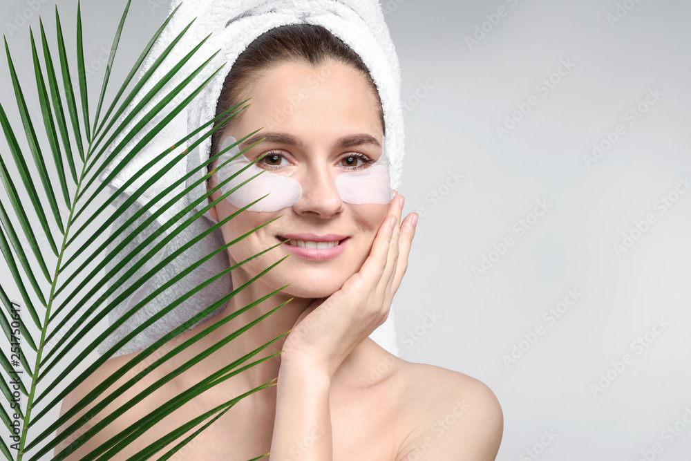 Woman with under-eye patches and tropical leaf on light background