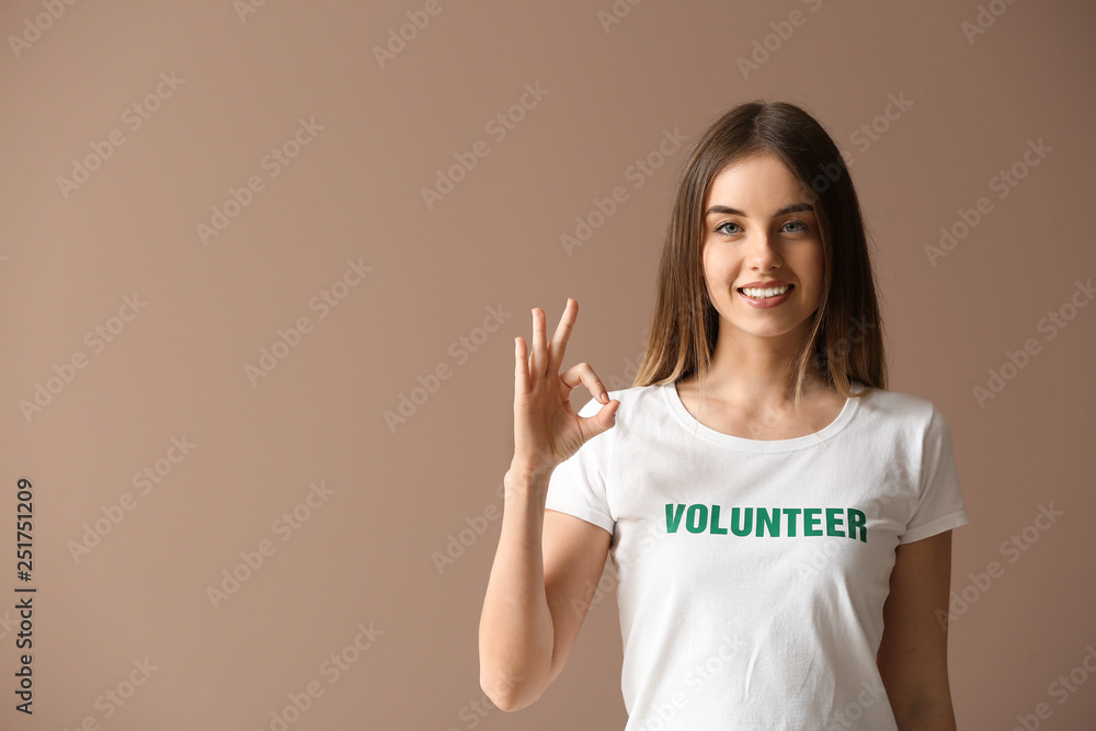 Young female volunteer showing OK on color background