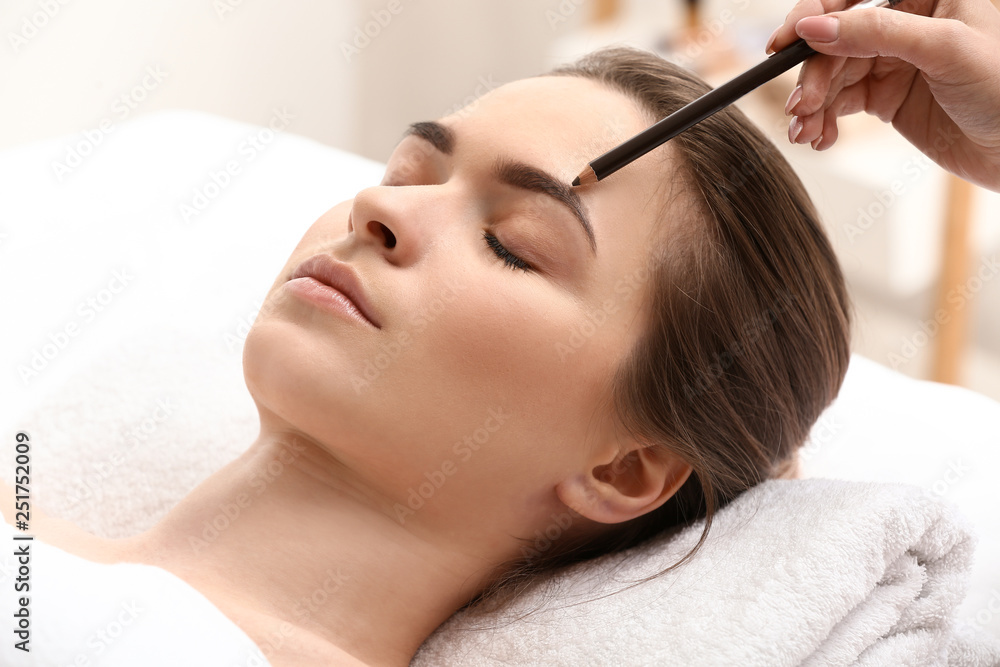 Young woman undergoing eyebrow correction procedure in beauty salon