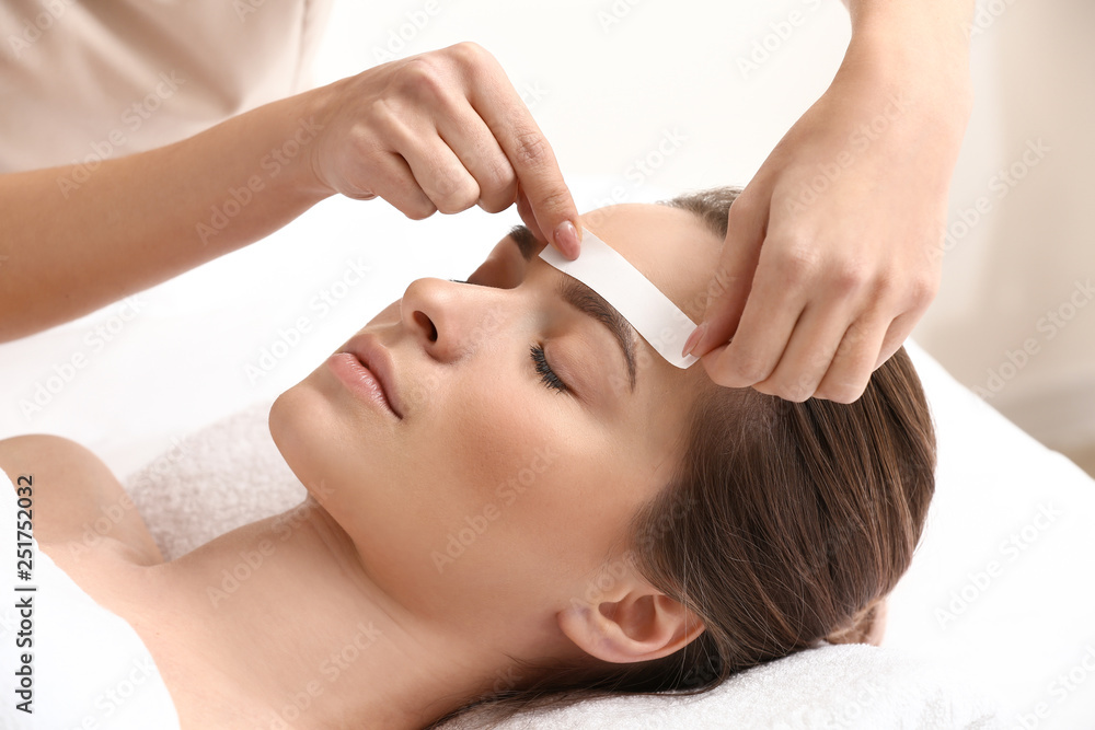 Young woman undergoing eyebrow correction procedure in beauty salon