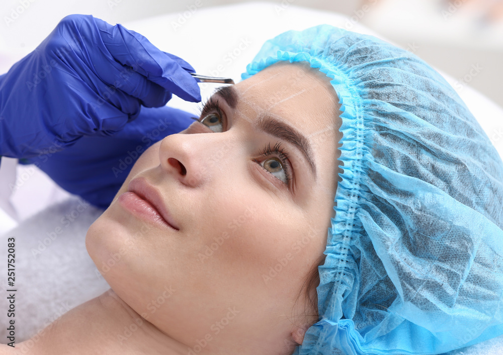 Young woman undergoing eyebrow correction procedure in beauty salon