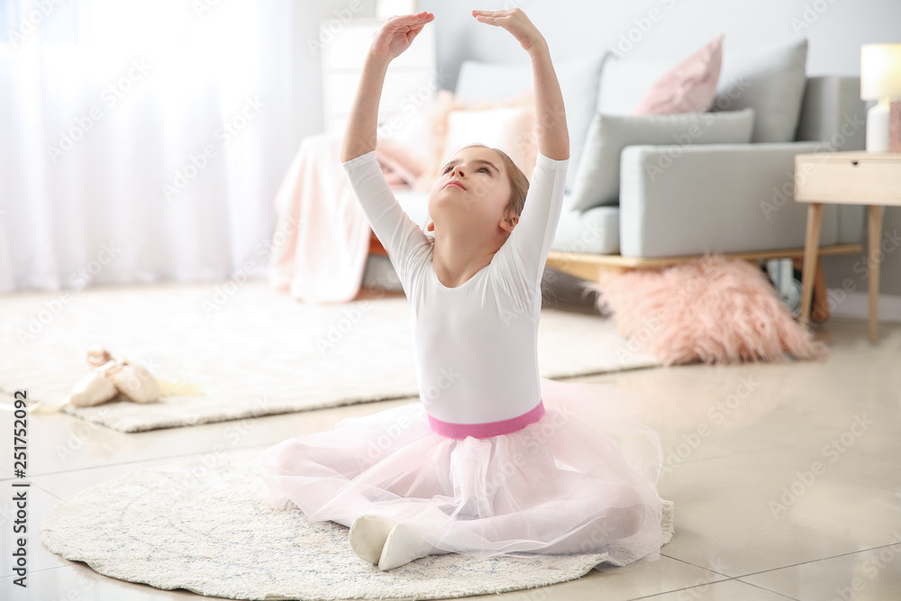 Cute little ballerina sitting on floor at home