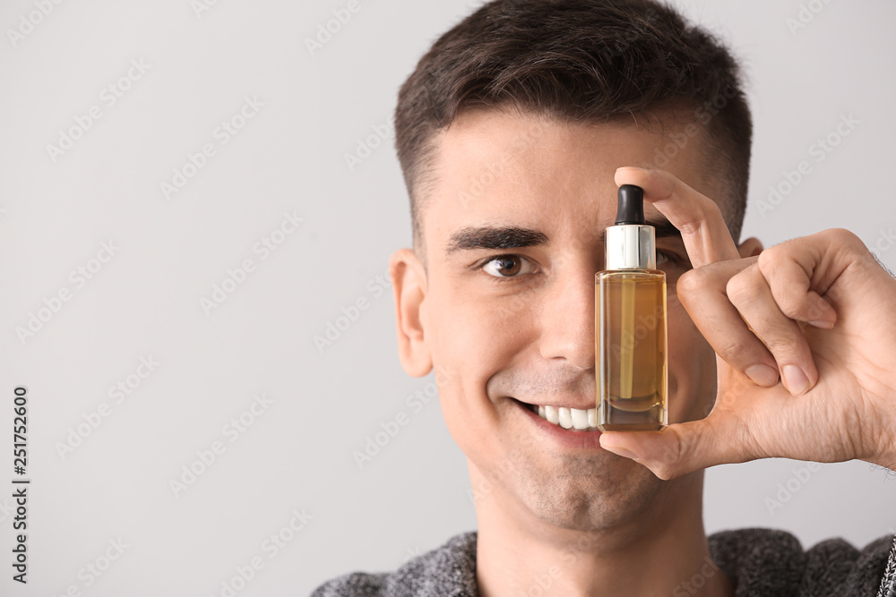 Handsome man with face serum on light background