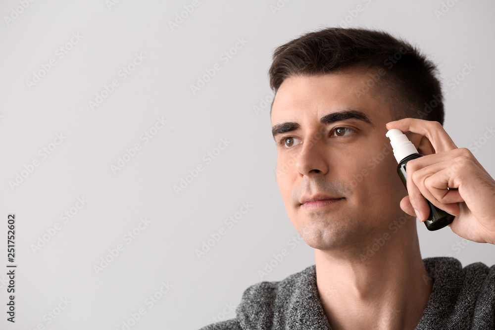 Handsome man with face serum on light background