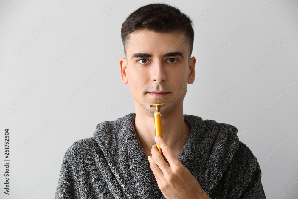 Man with facial massage tool on light background