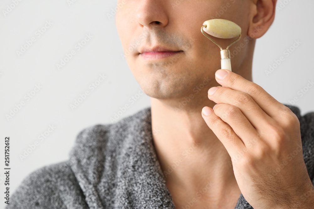 Man with facial massage tool on light background