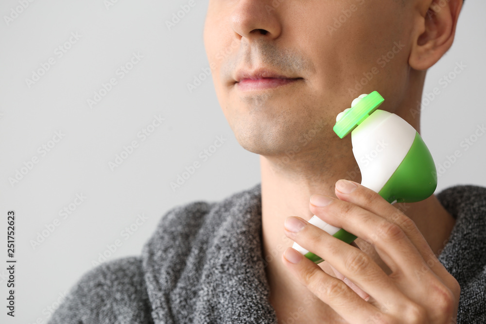 Man with facial massage tool on light background, closeup