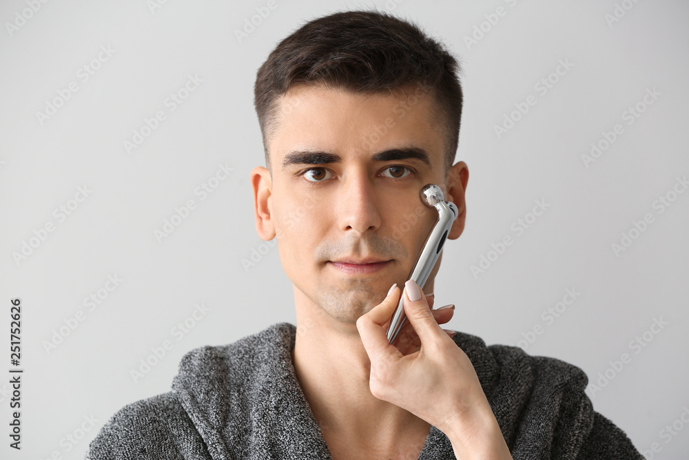 Man receiving facial massage on light background