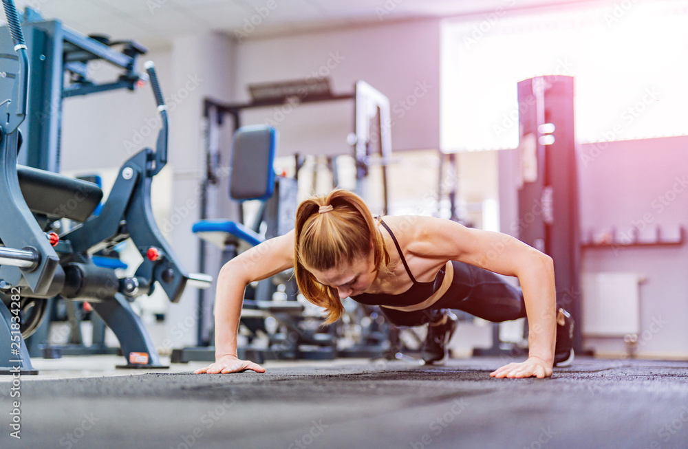 Strong young woman doing push-ups in gym. Young woman with muscular body. Fitness concept.