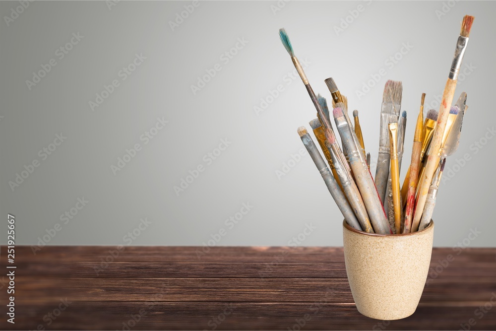 Brushes in a glass jar on the table and white wall