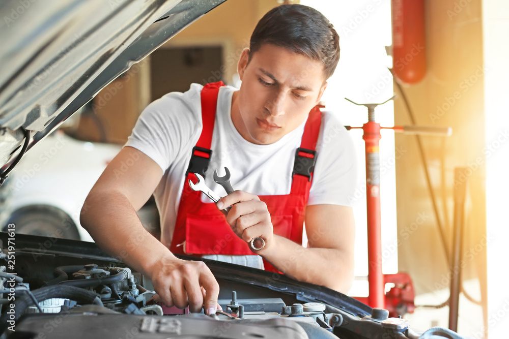 Young auto mechanic repairing car in service center