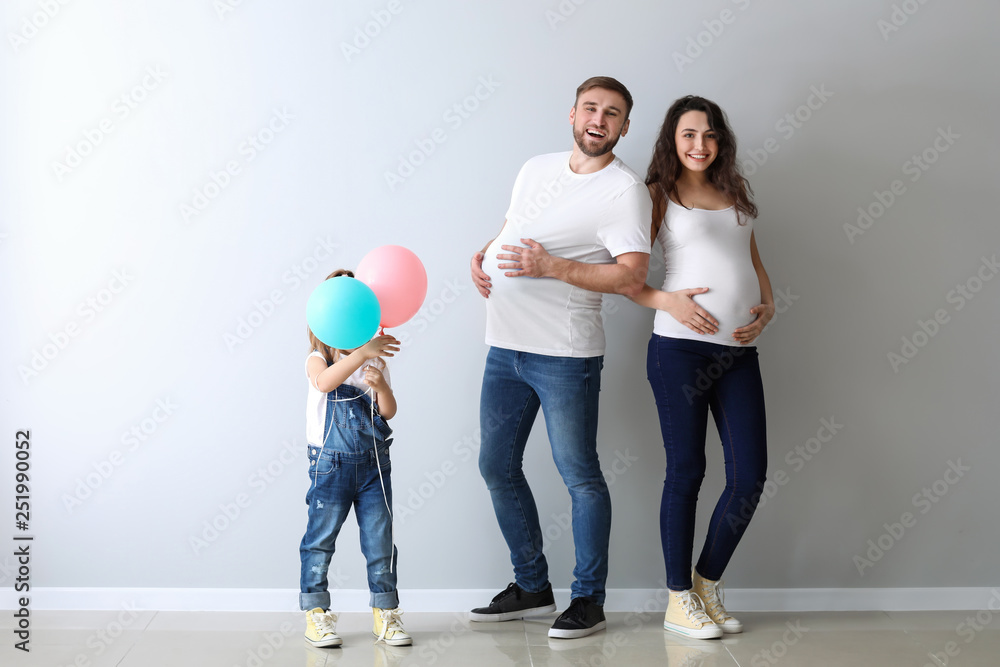 Happy family expecting baby near light wall