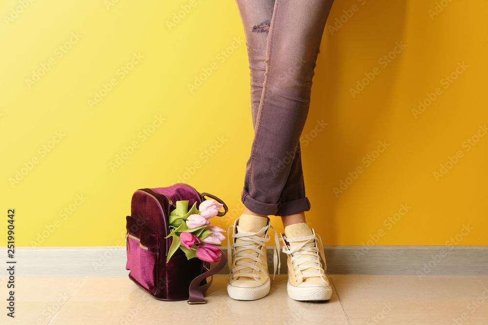 Beautiful young woman with backpack and bouquet of tulips near color wall