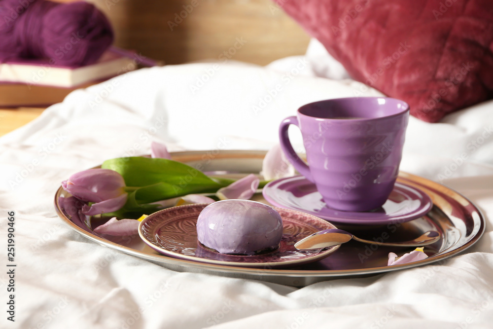 Tray with cup of coffee, cake and flower on bed