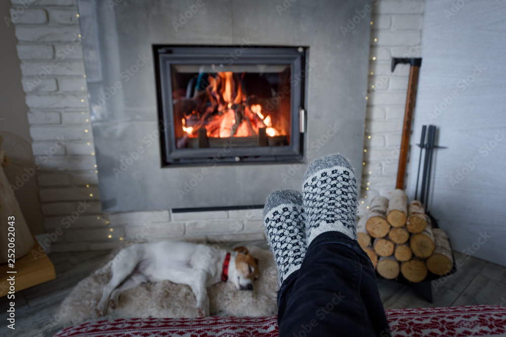 Burning fireplace and man feet in wool socks on foreground. Hygge concept