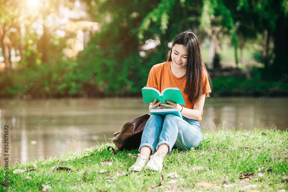 A young or teen asian girl student in university smiling and reading the book and look at the tablet