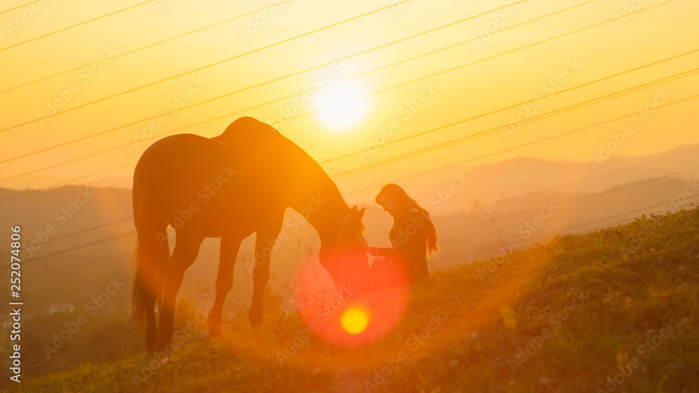 SUN FLARE: Happy young woman bonding with her stallion in a pasture at sunrise.