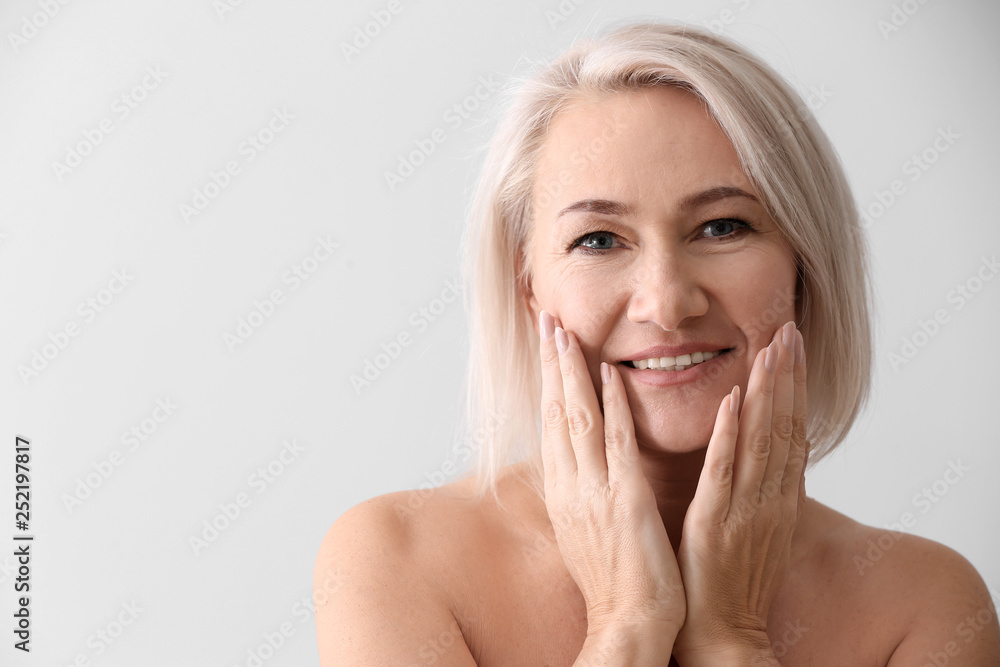 Mature woman giving herself face massage on light background